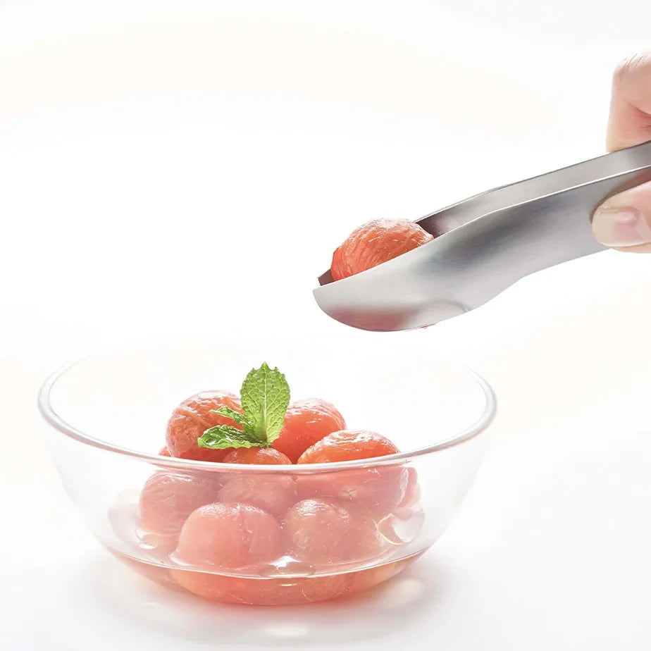Hasam S tongs serving melon balls from a glass bowl