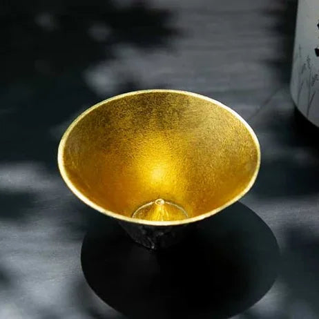 Gold-leaf FUJIYAMA cup on a black base beside a sake bottle