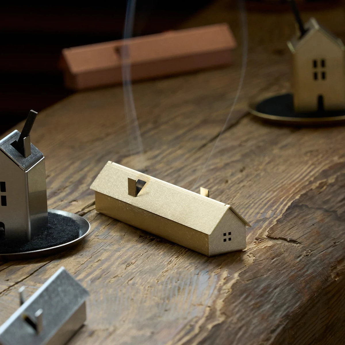 Brass, stainless steel and copper Incense House holders with smoke rising on a wooden table