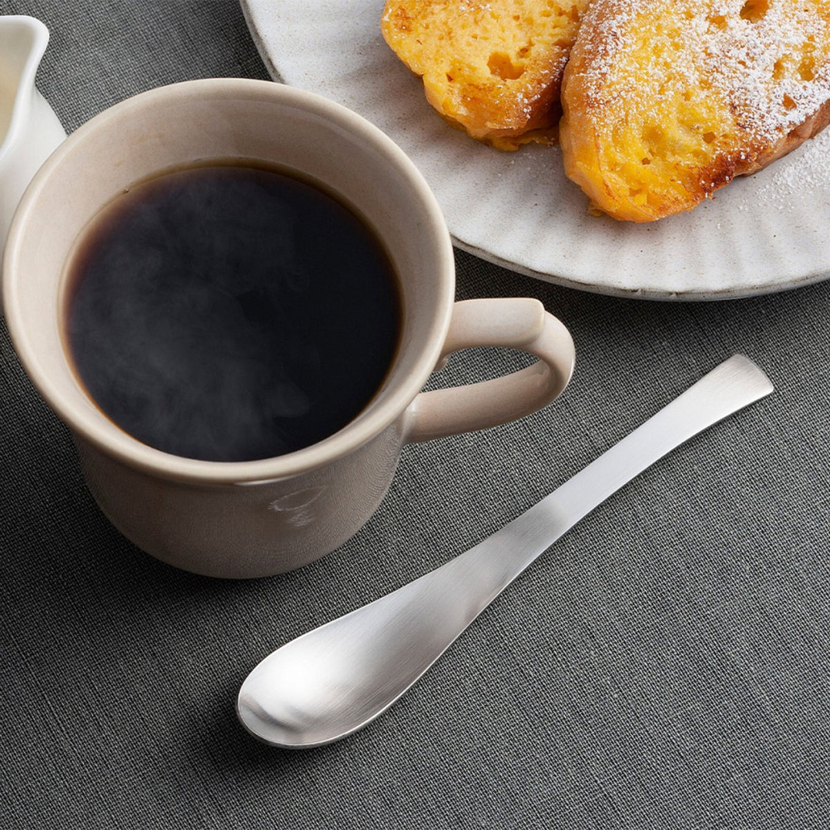 Mug spoon beside a cup of coffee and pastries